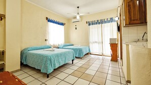 Una habitación con dos camas, una ventana con cortinas, un ventilador de techo y una pequeña cocina.