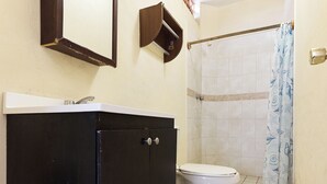 Un baño con tocador negro, inodoro, ducha con cortina y espejo en la pared.