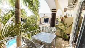 Un balcón con piscina, sillas blancas, una mesa y plantas diversas.