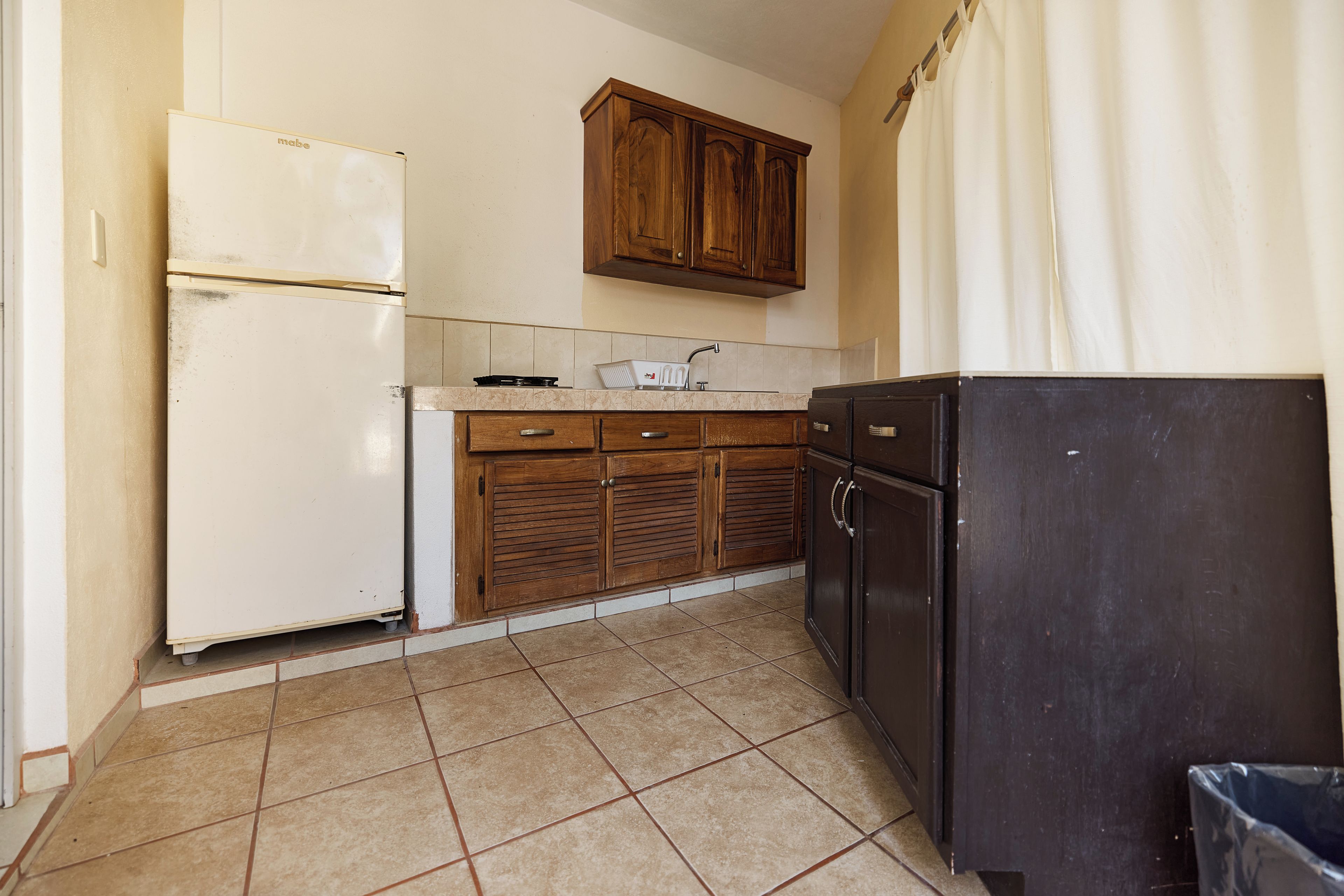 A kitchen with a refrigerator, stove, cabinets, and a trash bin.