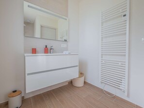 Et moderne badeværelse med et hvidt møbel, et spejl, et håndklædestativ og en radiator.