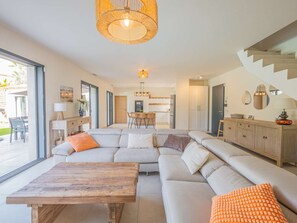 Een moderne woonkamer met een grote hoekbank, een houten salontafel, en een eethoek met een keuken op de achtergrond.