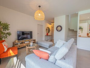 A modern living room with a grey sofa, a television, and a hanging light fixture. - Spacious property with 2 villas and swimming pool – Grimaud (GRIMAUD)