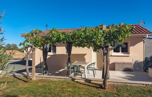 A house with a covered patio, a table with chairs, and a pergola with vines. - Charmant gîte au calme (La Douze)