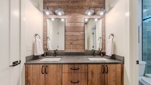 A modern bathroom with wooden cabinetry, two sinks, and a large mirror with overhead lighting. - Arctic Fox - Yellowstone Getaway! (Island Park)