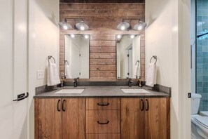 Ein modernes Badezimmer mit Holzschränken, zwei Waschbecken und einem großen Spiegel mit Deckenleuchten.