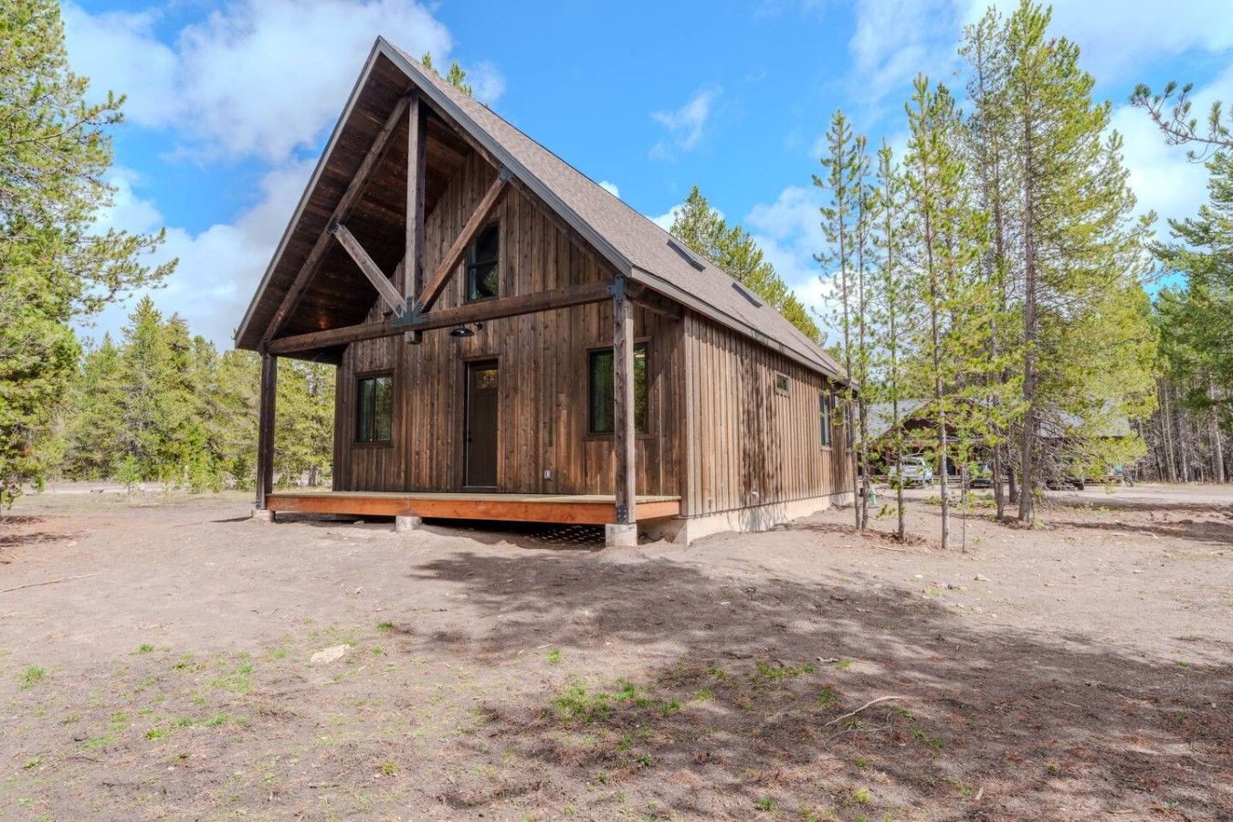 A wooden cabin with a gabled roof, a porch, and a dirt ground.
