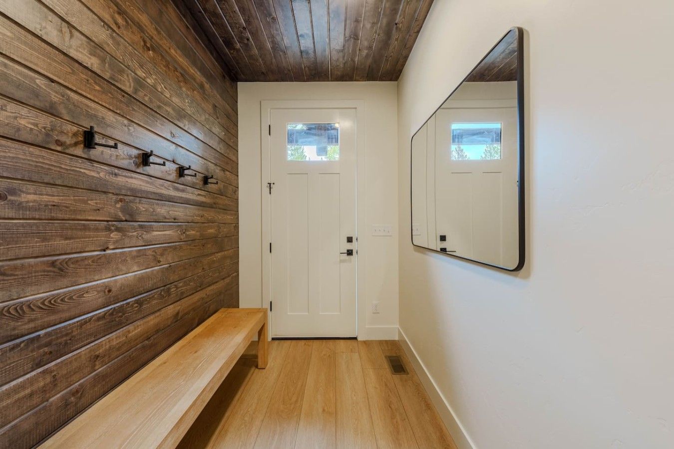 A hallway with wooden paneling, a bench, a white door, and a mirror on the wall.