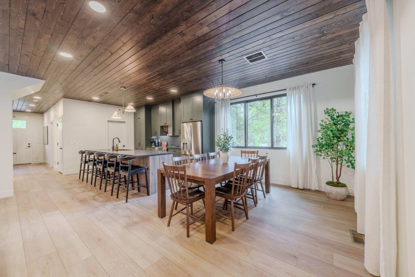 A spacious kitchen with wooden ceiling beams, a central island with bar stools, and a dining area with a large wooden table and chairs.