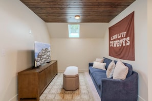 A room with a wooden ceiling, a mounted television, a blue sofa, and a flag with text. - Arctic Fox - Yellowstone Getaway! (Island Park)