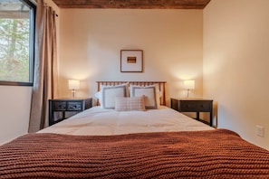 A bedroom with a bed, two bedside tables, a window with curtains, and a wooden ceiling. - Arctic Fox - Yellowstone Getaway! (Island Park)