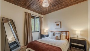 A bedroom with a bed, bedside tables, a mirror, and a window with curtains. - Arctic Fox - Yellowstone Getaway! (Island Park)