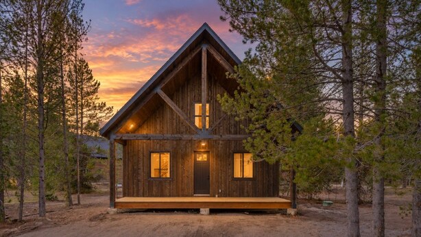 A wooden cabin with a prominent gable roof, a front porch, and a dirt driveway surrounded by trees. - Arctic Fox - Yellowstone Getaway! (Island Park)