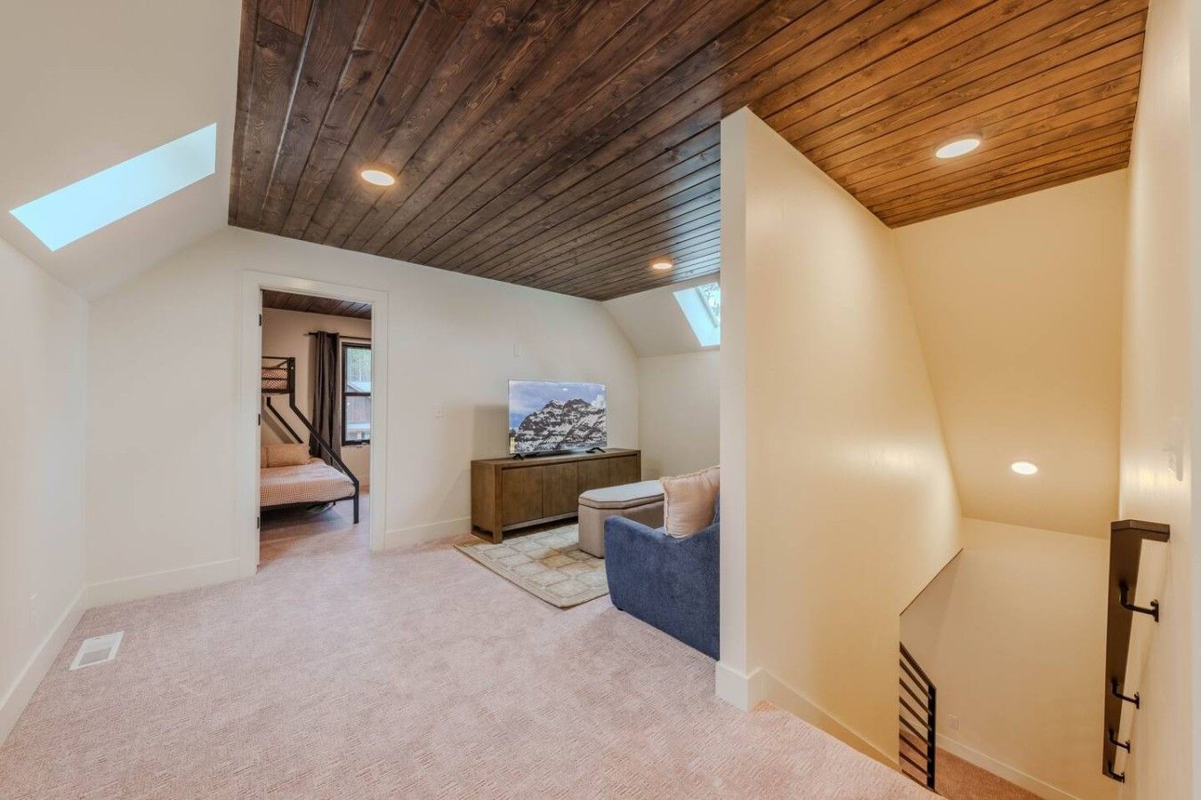 A spacious attic room with a sloped ceiling, a built-in TV, a cozy seating area, and a staircase leading to the upper floor.