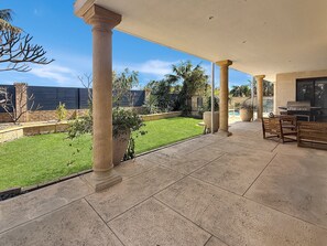 A covered patio area with a view of a well-maintained lawn and a pool. - Beachside 4-Bed House With Pool In Warnbro (Warnbro)