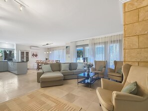 Een ruime woonkamer met een hoekbank, een salontafel en een eethoek met stoelen en een tafel.