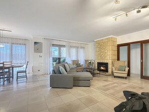 Een ruime woonkamer met een hoekbank, een open haard en een eethoek met een tafel en stoelen.
