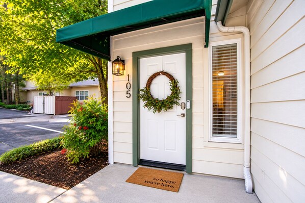 A residential house with a white door, number 105, a green awning, a wreath, and a doormat with a welcoming message.