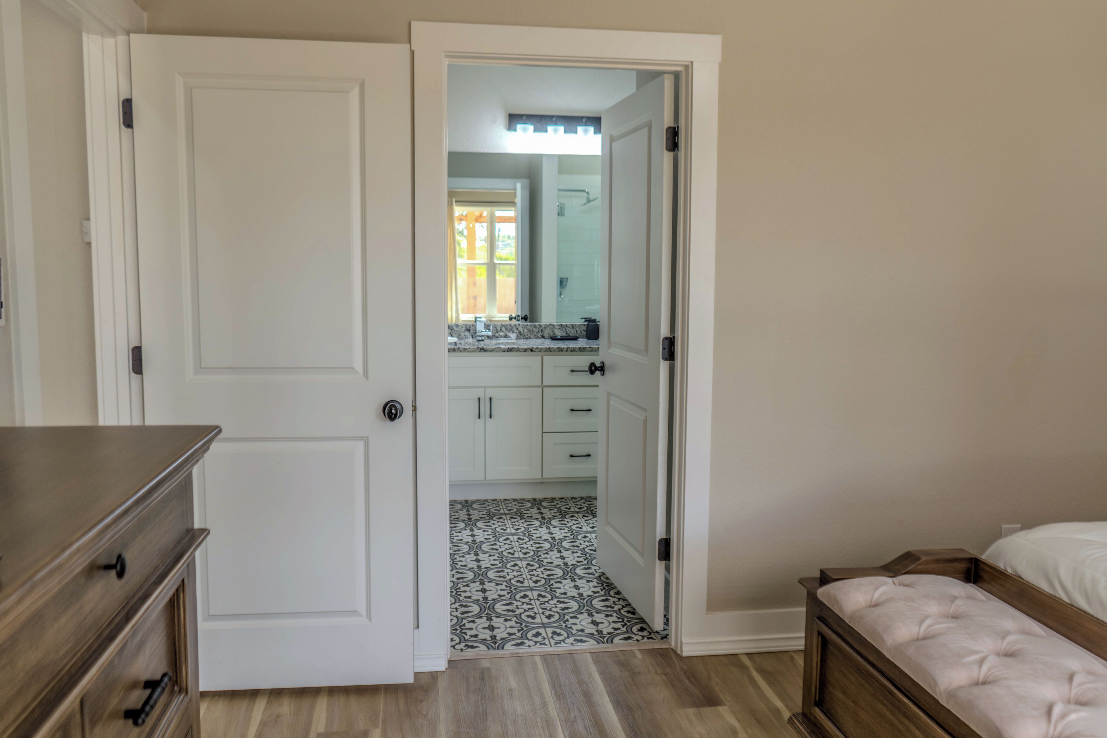 Une chambre à coucher avec une commode en bois, un lit doté d’une tête de lit et une salle de bain visible à travers une porte ouverte.