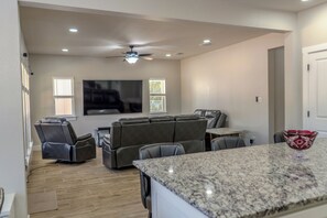A spacious living room with a large flat-screen TV, a ceiling fan, and a seating area with a marble countertop.
