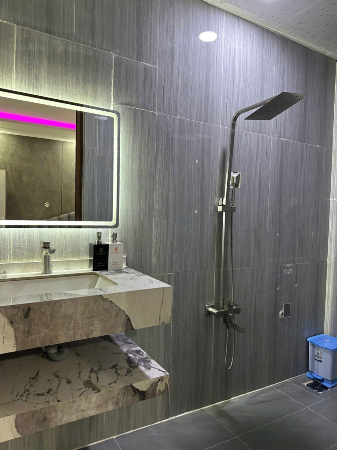 Un baño moderno con lavamanos de mármol, un espejo grande y una ducha.