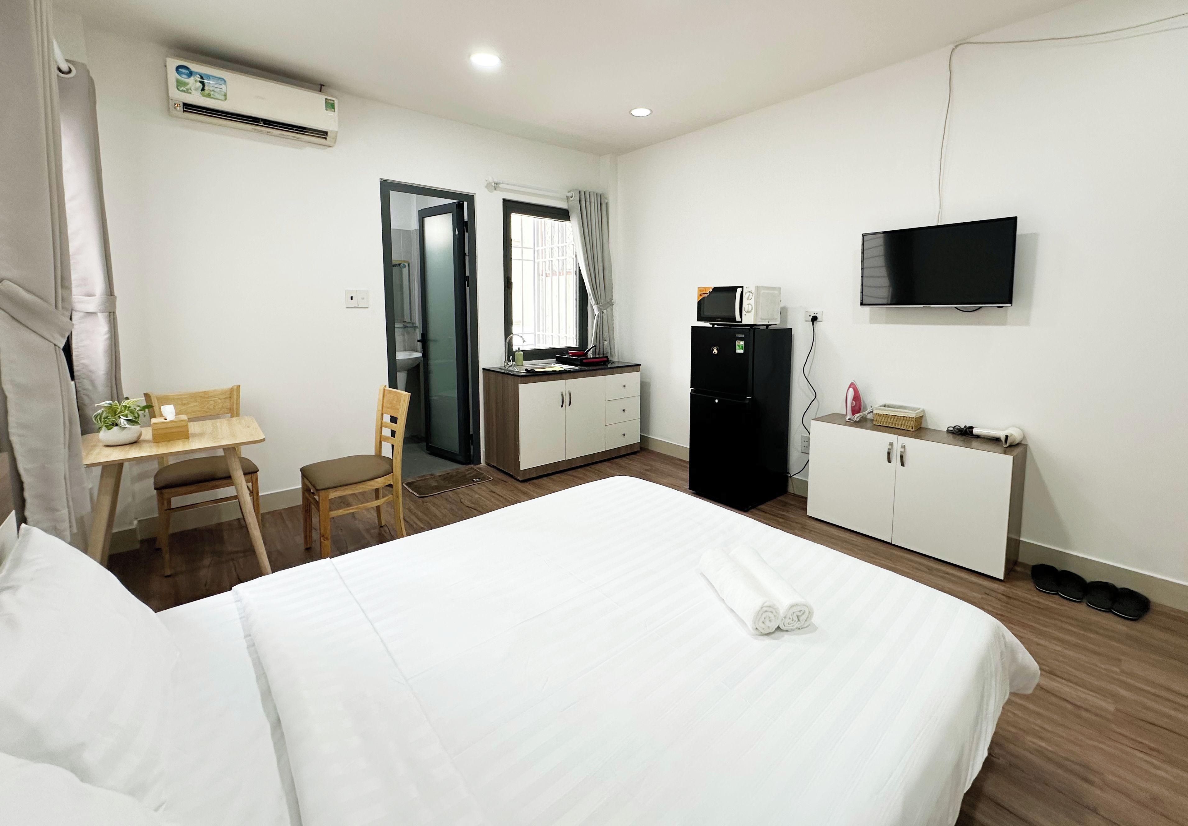 Una habitación de hotel con cama, escritorio, silla, armario, televisor y microondas.