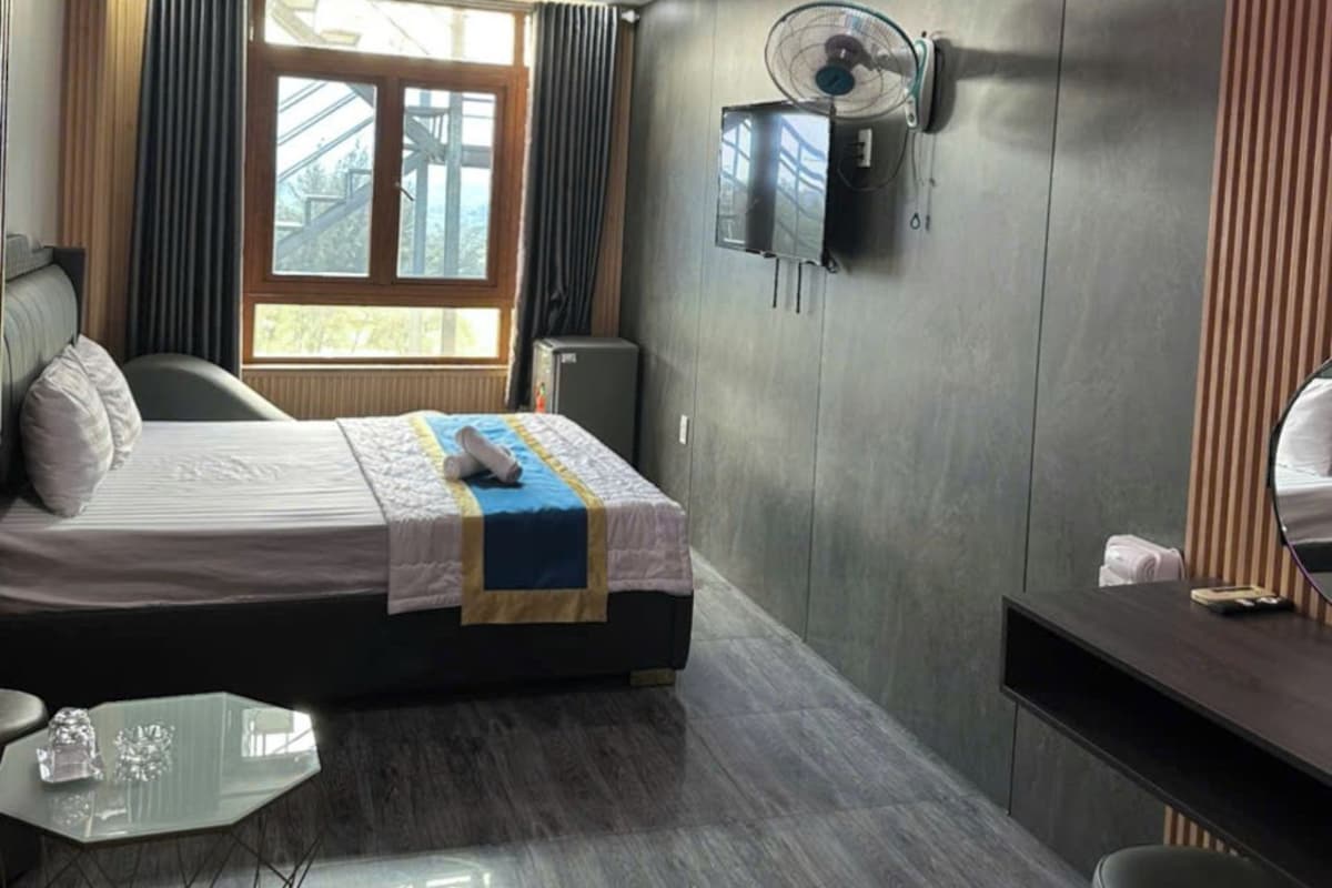 A modern hotel room with a bed, a desk, a fan, and a TV mounted on the wall.