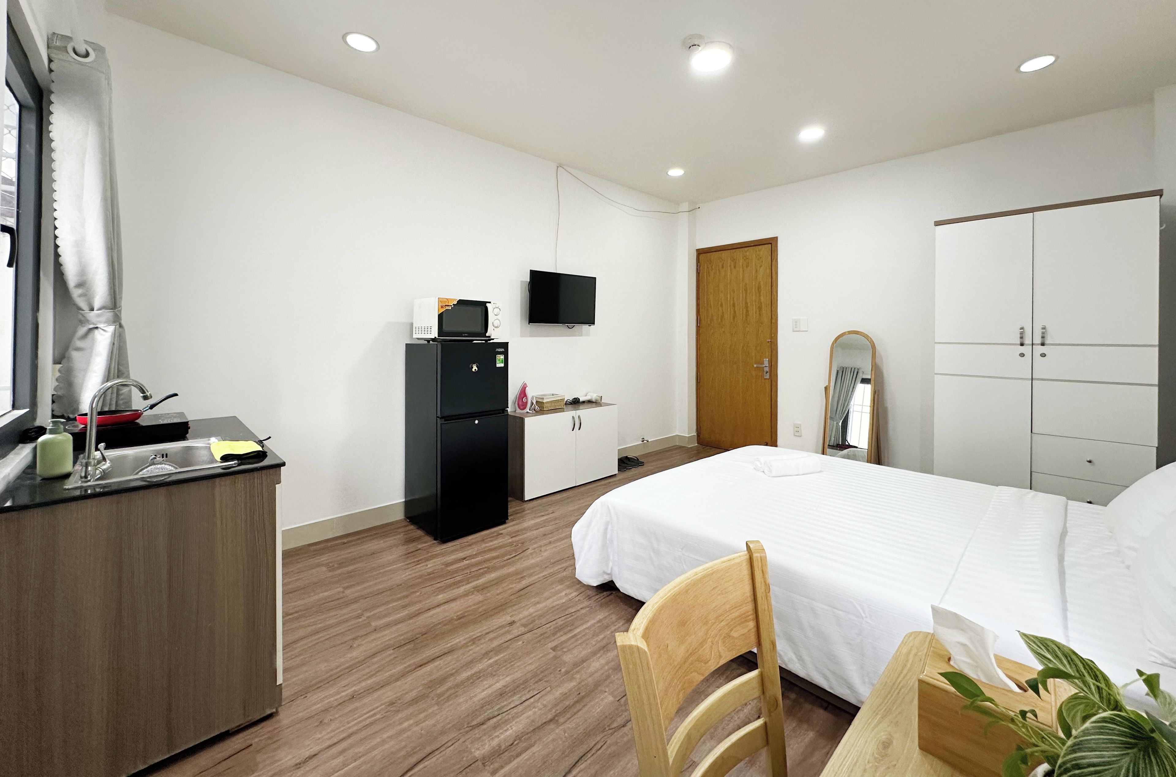 Habitación de hotel con cama, escritorio, lavamanos, televisor, armario y puerta.
