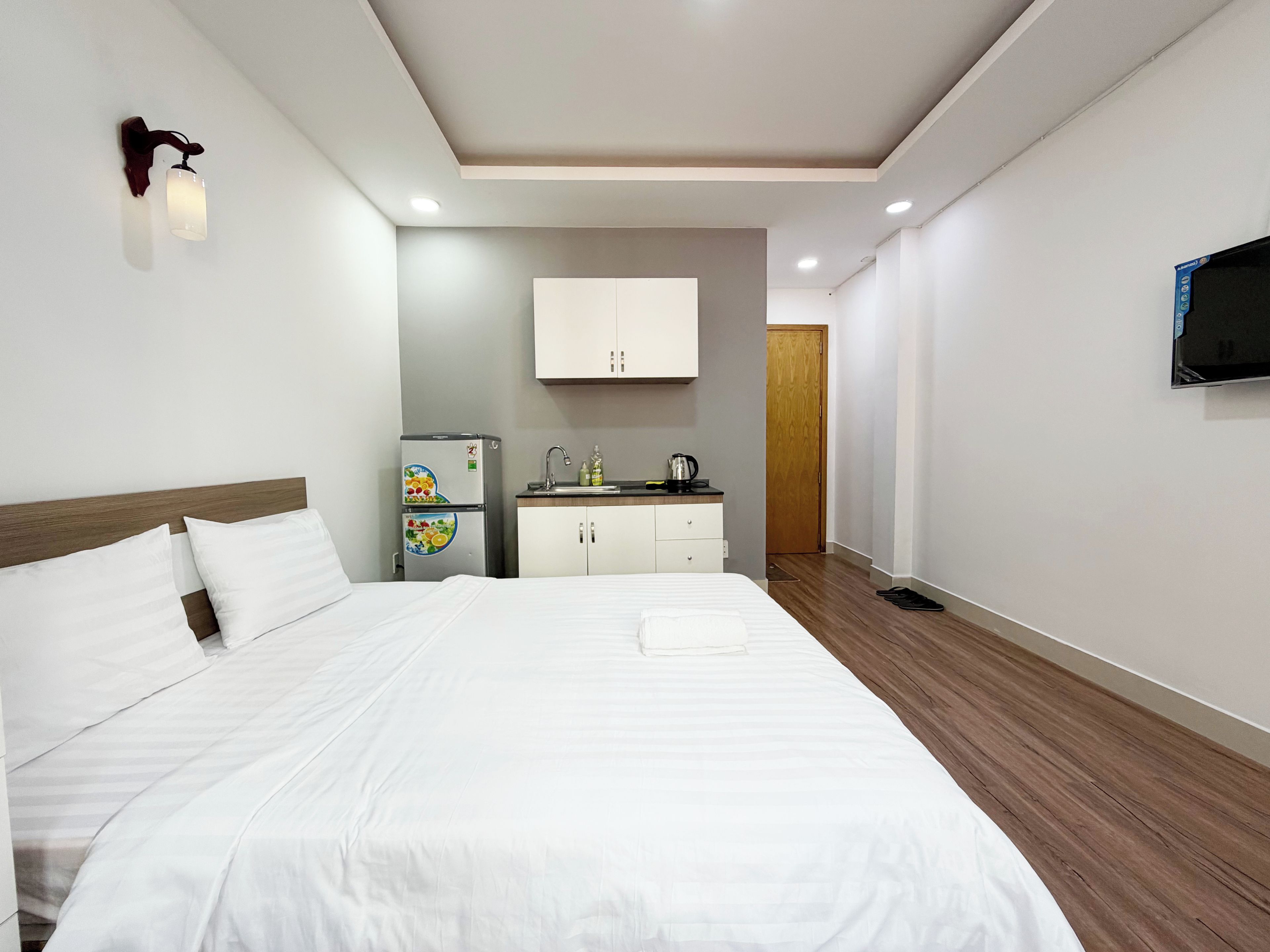 Ein Hotelzimmer mit Bett, einer Küchenzeile, einem an der Wand montierten Fernseher und Holzboden.