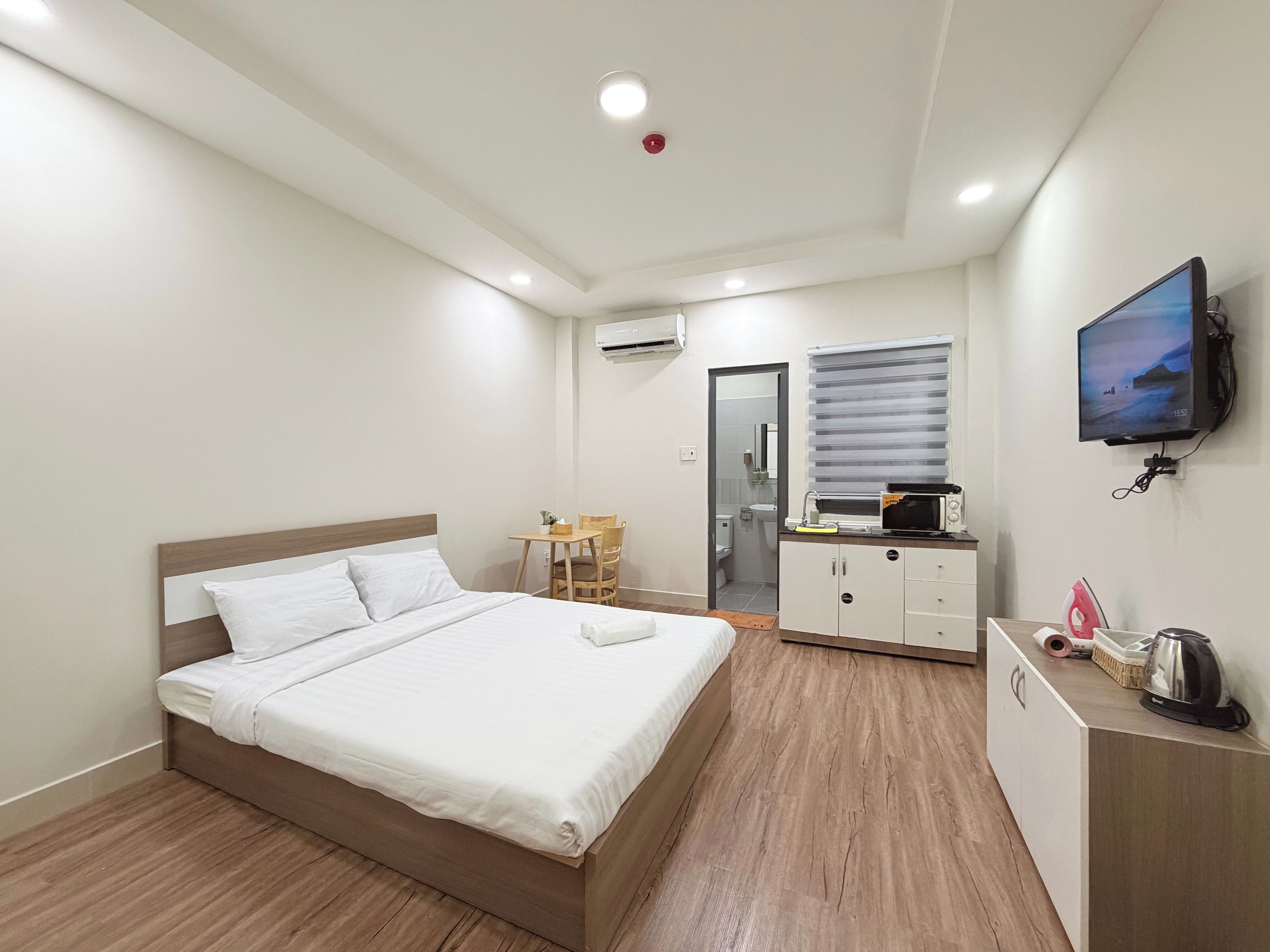 Una habitación de hotel con cama, una mesita, televisor y kitchenette.