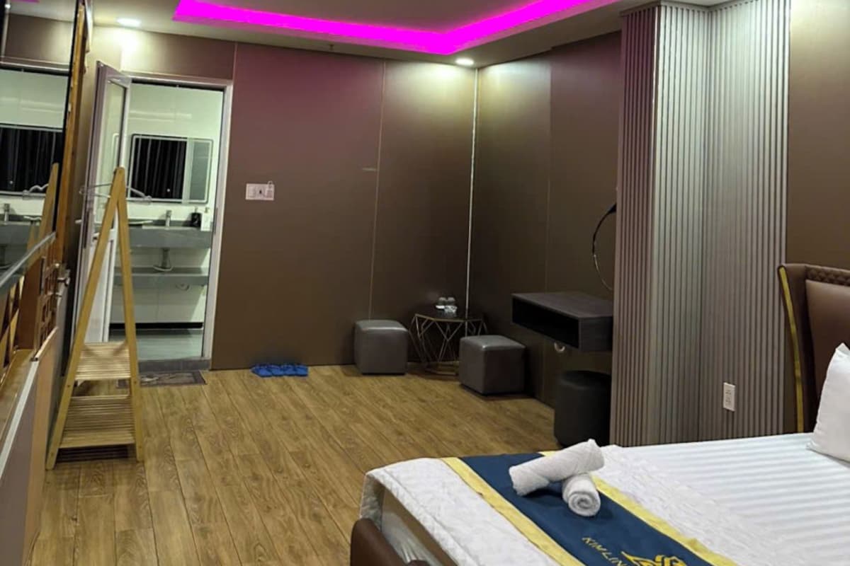 A hotel room with a bed, a desk, a chair, a standing fan, and a mirror.