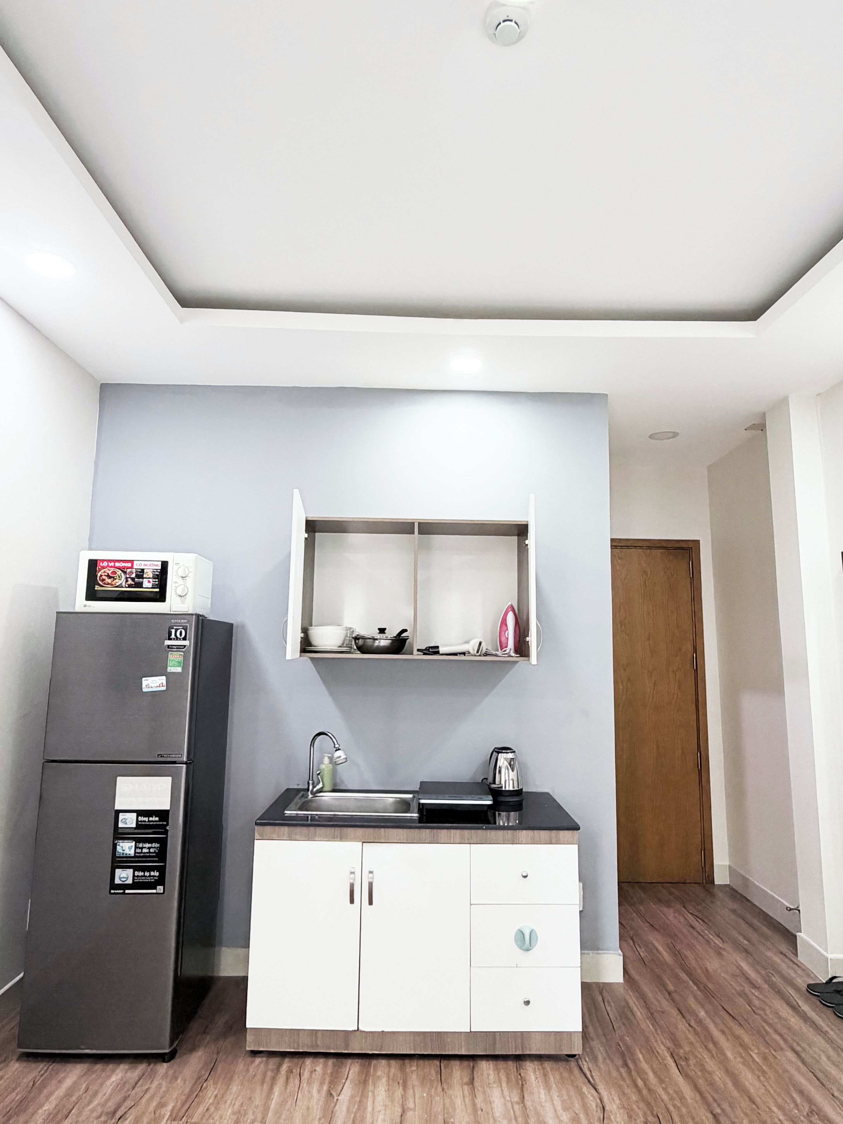 Una kitchenette compacta con refrigerador, microondas, lavamanos y alacenas.