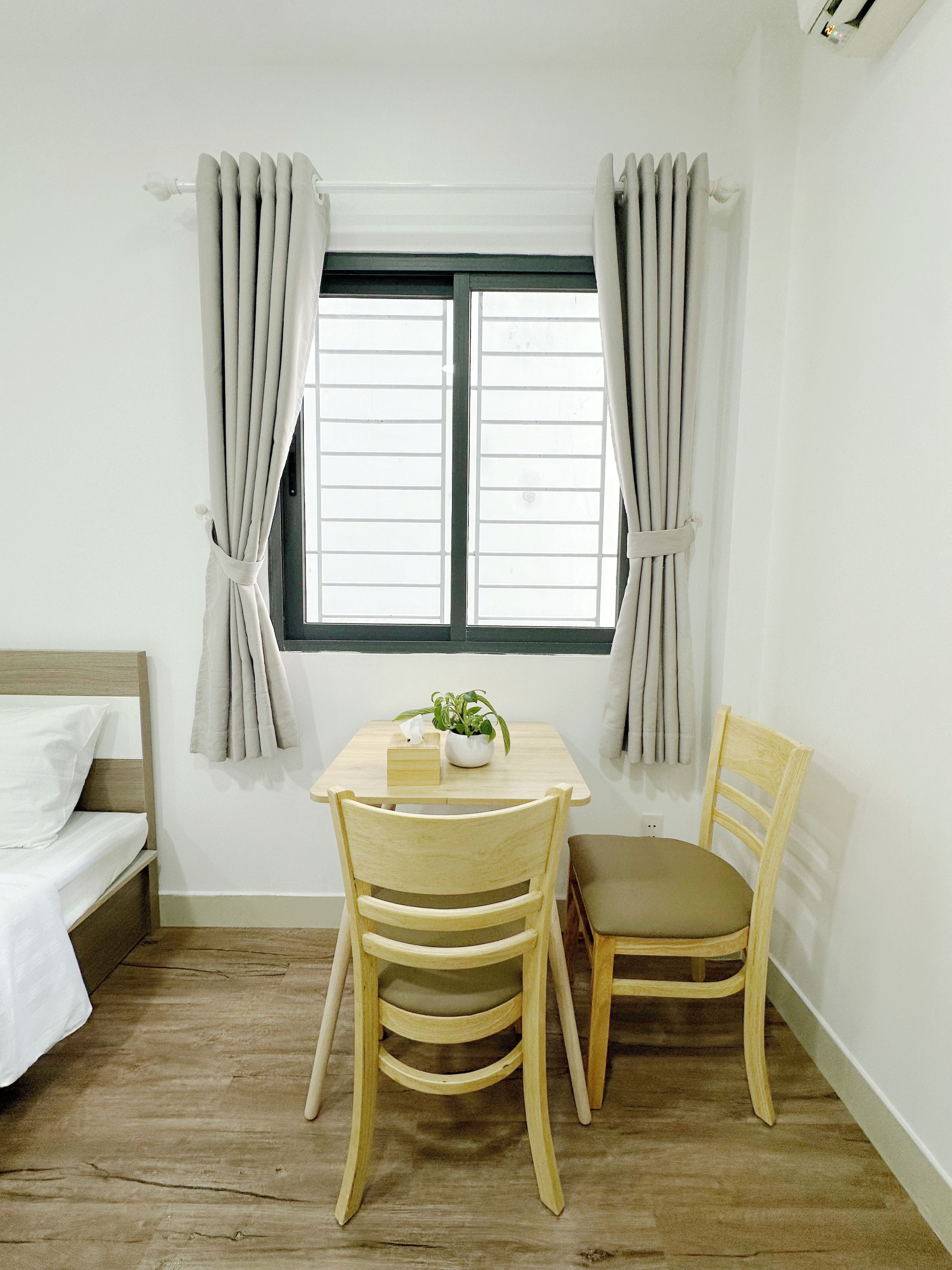 Una habitación pequeña con una cama, una mesa con una planta y dos sillas.