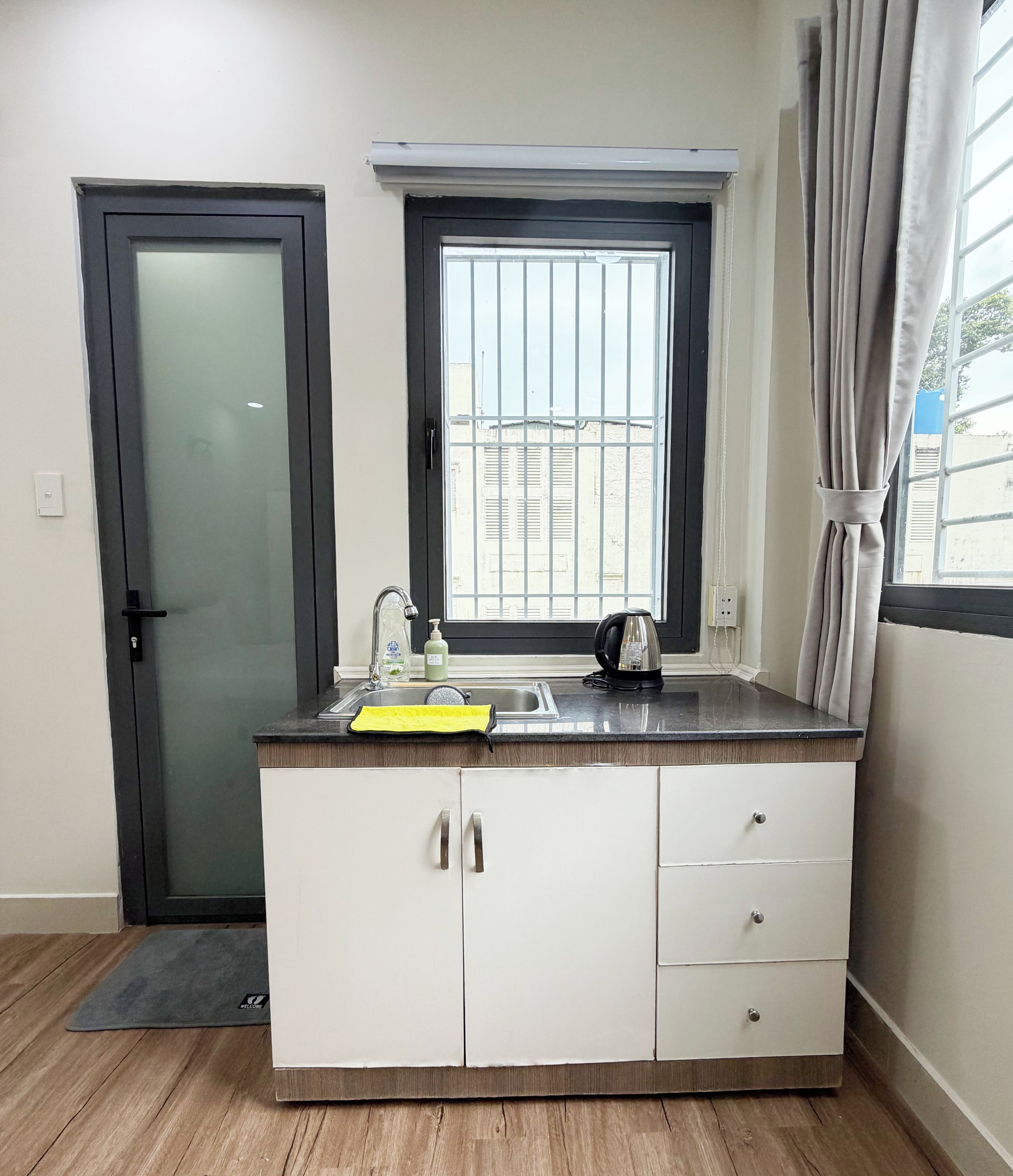 Una cocina compacta con un lavamanos empotrado, una ventana con rejas y una tetera sobre la encimera.