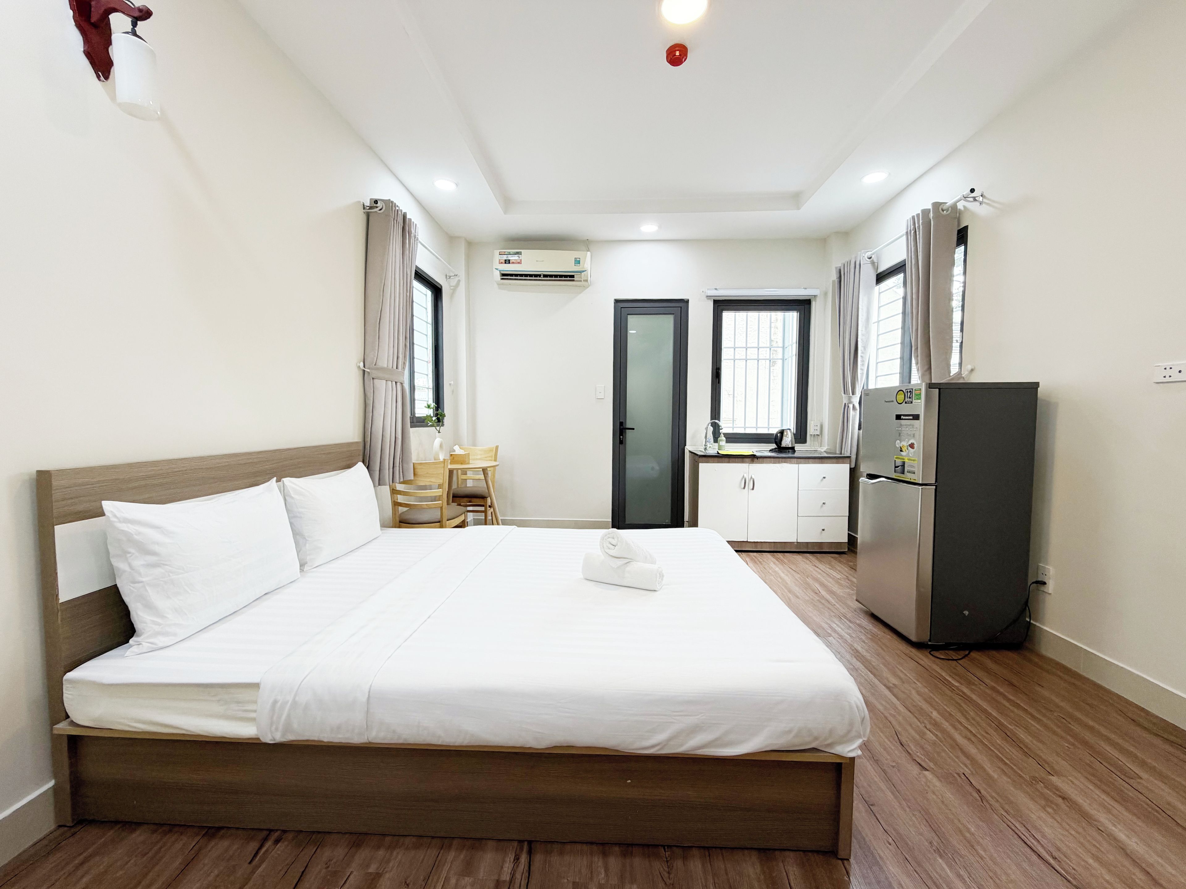 Una camera d'albergo con un letto, un tavolino, una sedia, un angolo cottura e un condizionatore d'aria.