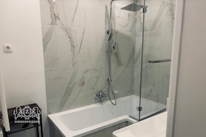 Ein Badezimmer mit einer gläsernen Duschkabine, einer weißen Badewanne und Marmorwänden.