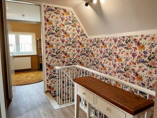 A room with a wooden bench, a white railing, and a floral wallpaper.
