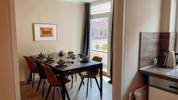 A dining area with a table set for four, chairs, a framed picture on the wall, and a view through a window.