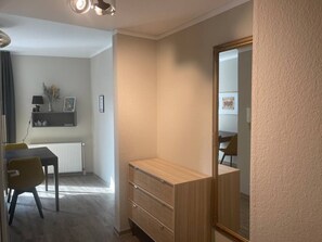 A room with a dining table, chairs, a mirror, and a small wooden cabinet.