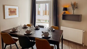 Ruokailutila, jossa on neljälle katettu pöytä, patteri, hylly lamppuineen ja seinällä oleva kehystetty kuva.