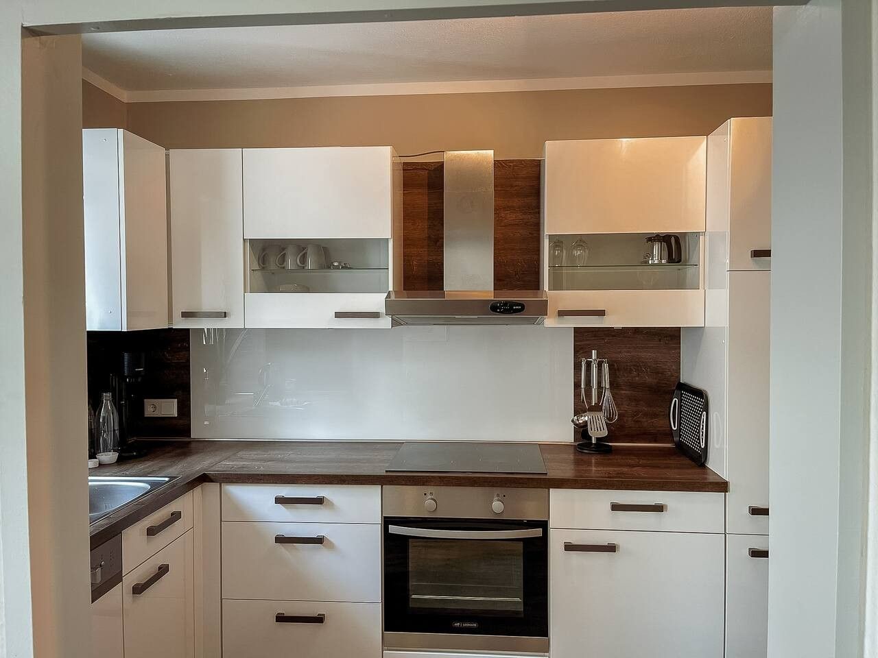 Une cuisine compacte avec des meubles blancs, un four encastré et un plan de travail en bois.