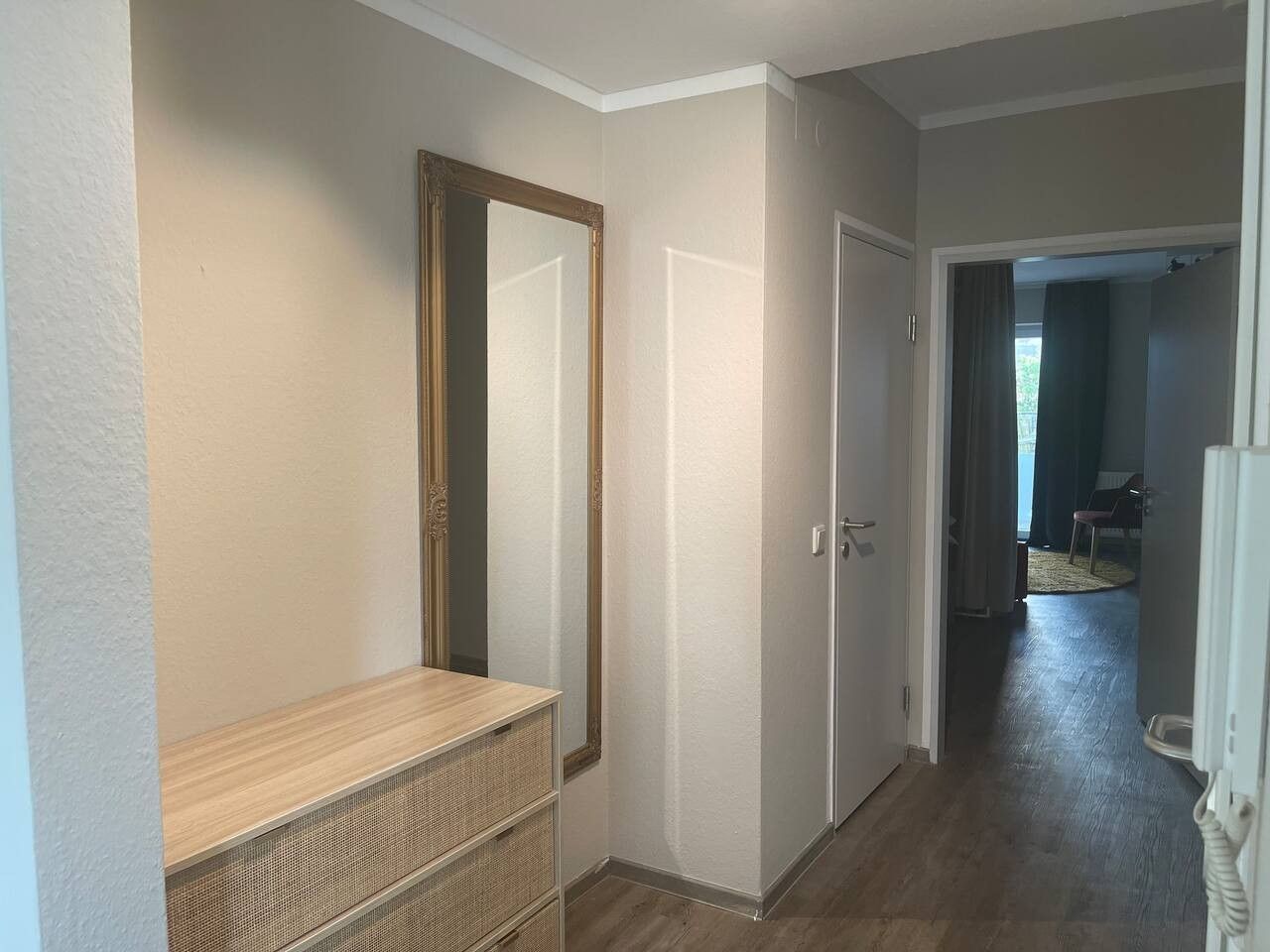 A hallway with a wooden bench, a large mirror, and a door leading to another room.