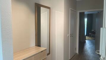 A hallway with a wooden bench, a large mirror, and a door leading to another room.