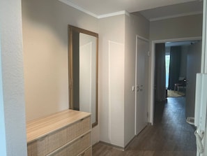 A hallway with a wooden bench, a large mirror, and a door leading to another room.