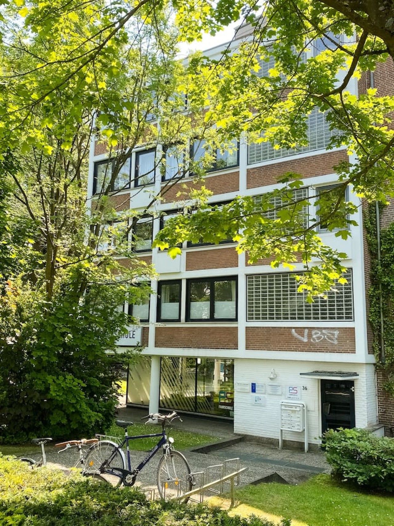 Un edificio a più piani con facciata in mattoni, ampie finestre e una bicicletta parcheggiata davanti.
