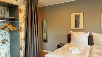 Een hotelkamer met een bed, een kledingkast, een spiegel en een kunstwerk in een lijst aan de muur.