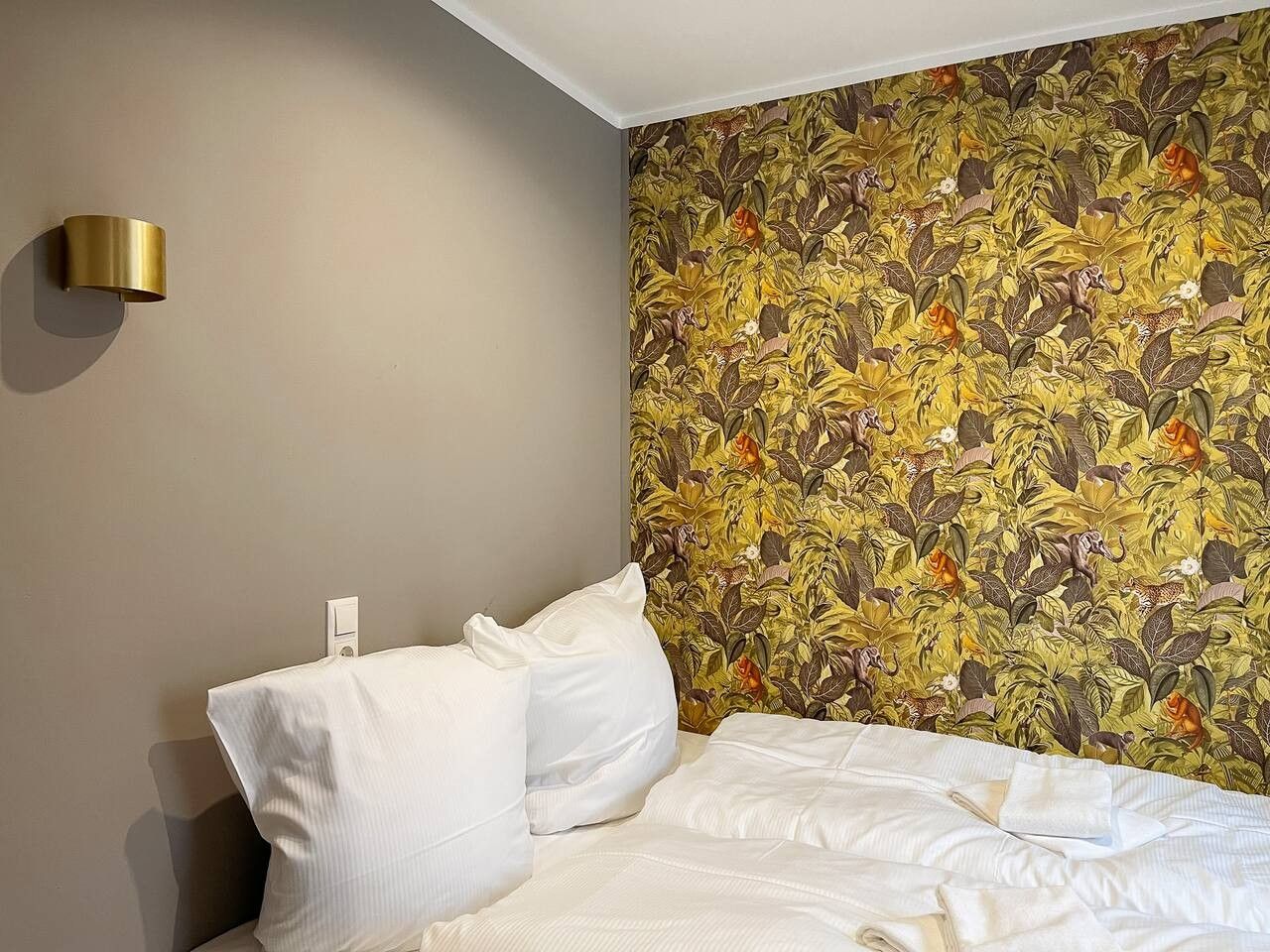 Ein Hotelzimmer mit einem Bett, weißer Bettwäsche, einer Wandleuchte und floralem Wandpapier.