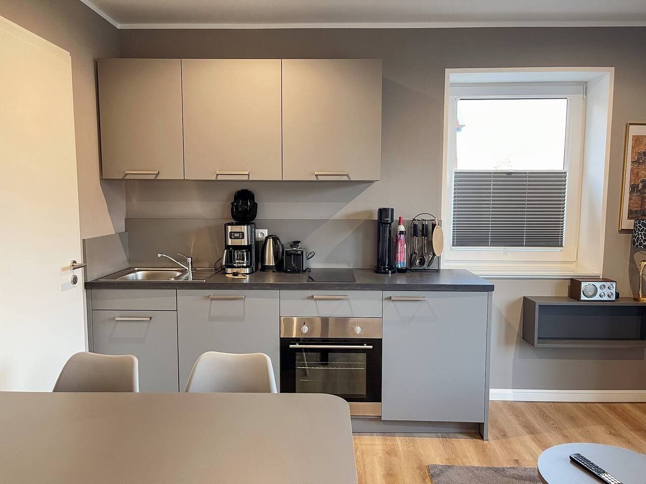 Una cocina compacta con electrodomésticos modernos, horno integrado y ventana con persianas.