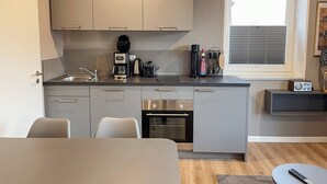Cozinha compacta com eletrodomésticos modernos, forno embutido e janela com persianas.