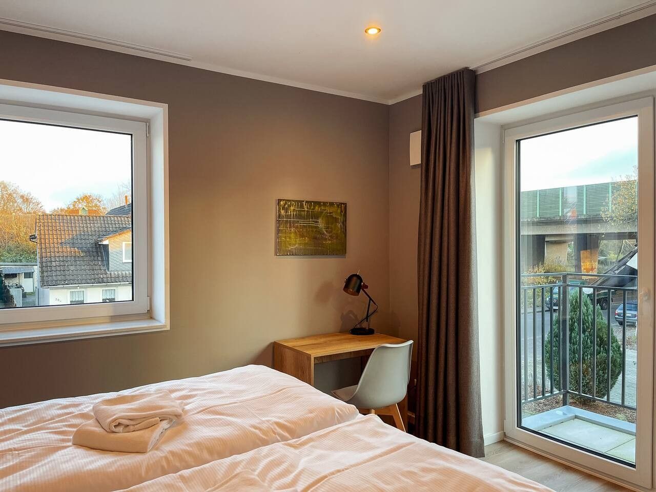 Ein Hotelzimmer mit Bett, Schreibtisch, Stuhl und Blick auf einen Balkon.